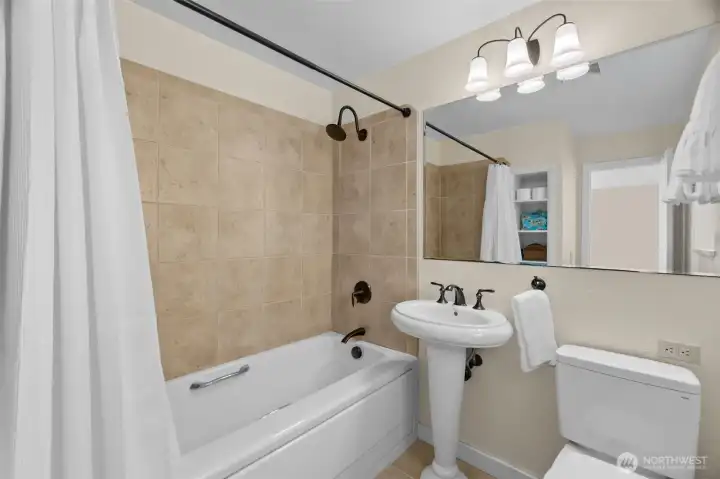 Primary bathroom is fresh and bright as well; tiled shower, large mirror, and built-in storage, with privacy window for natural light.