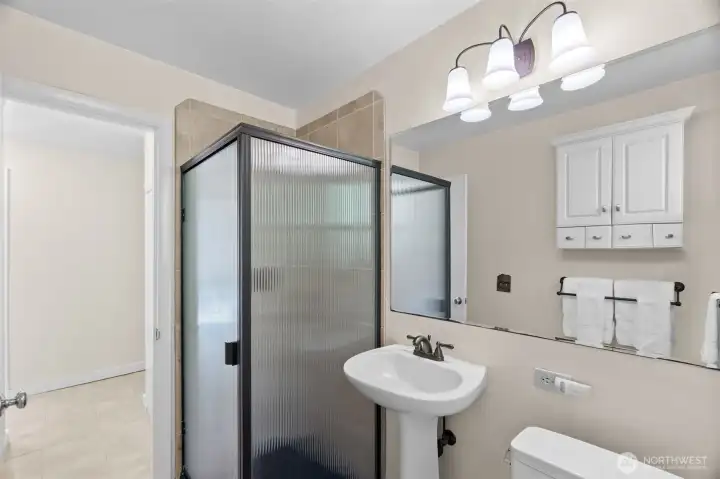 Hall bath for guests/family continues the fresh feel with tiled shower, large mirror, and pedestal sink; built-in linen cabinet just outside the doorway in the hall; privacy window allows for more natural light.