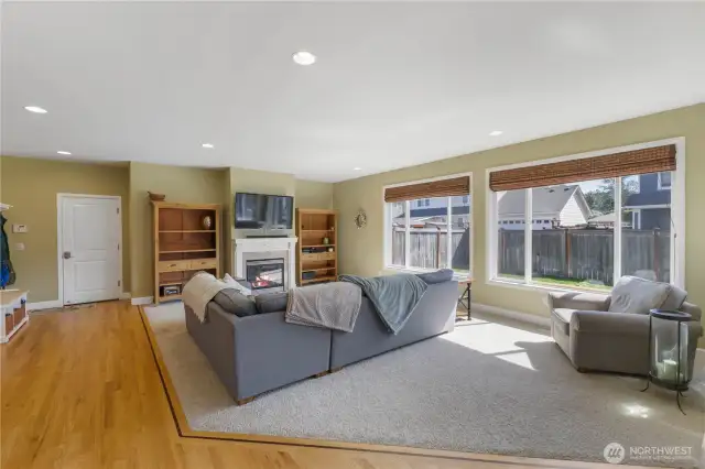 The great room offers a comfortable and inviting space with a cozy gas fireplace framed by a classic white mantle and tile surround. Large windows provide plenty of natural light and a lovely view of the fenced, landscaped backyard.