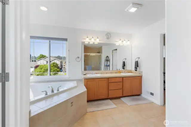 The primary bathroom offers a spa-like experience with a large soaking tub, separate shower, and tile work throughout. Double sinks and generous cabinet and counter space provide both luxury and everyday convenience.