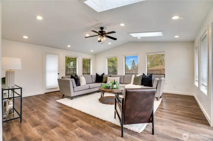 Bright, airy family room with vaulted ceiling, skylight, and two doors opening to outdoor spaces—flooded with natural light.