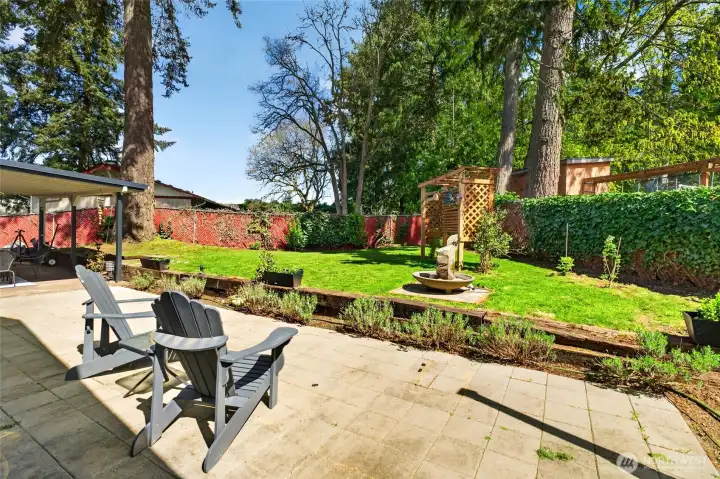 Private, fully fenced backyard retreat featuring a covered patio with additional stonework to expand the entertaining space, room for gardening, and has the addition of a charming arbor perfect for hanging bird feeders.