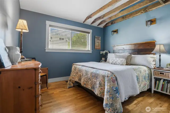 Spacious, light-filled bedroom conveniently located off the main living area, featuring beautiful hardwood flooring and charming architectural accent beams. Spacious, light-filled bedroom conveniently located off the main living area, featuring beautiful hardwood flooring and charming architectural accent beams.