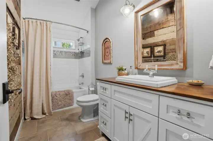 This guest bathroom, featuring expansive vaulted ceilings that create an airy and inviting atmosphere. The space is beautifully appointed with an elegant vanity and a pristine tiled bath/shower combination, complemented by durable and stylish tile flooring. Thoughtfully placed barnwood accents provide a touch of rustic charm, adding unique character and warmth to the this space. This guest bathroom, featuring expansive vaulted ceilings that create an airy and inviting atmosphere. The space is beautifully appointed with an elegant vanity and a pristine tiled bath/shower combination, complemented by durable and stylish tile flooring. Thoughtfully placed barnwood accents provide a touch of rustic charm, adding unique character and warmth to the this space.
