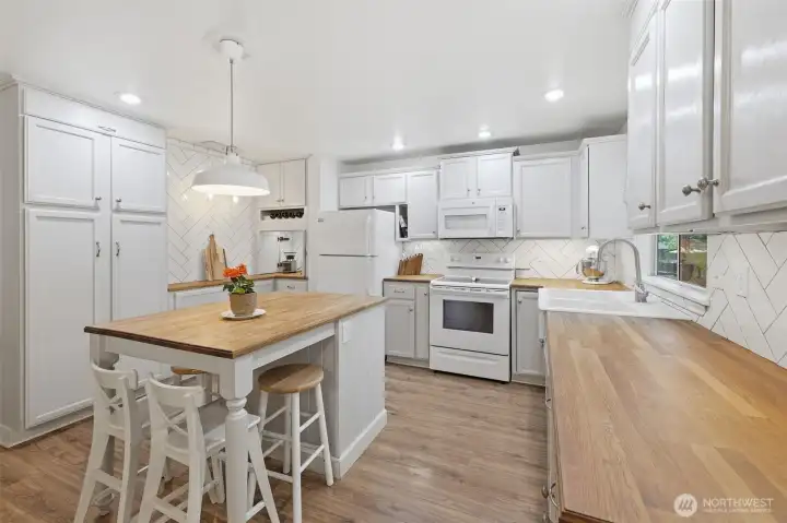 Butcher block countertops, recessed lighting, extra storage, breakfast island, and beautiful herringbone tiling make it easy to be creative in this kitchen.