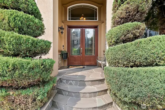 Grand wide stone entryway leads to custom double wood doors.
