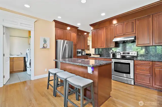 A gourmet kitchen featuring granite countertops, beautifully stained wood cabinetry, a generous walk-in pantry with ample storage and plenty of counterspace. The open layout showcases a casual eating area, family room and outdoor deck.  All of the newer Stainless Steel appliances are included.