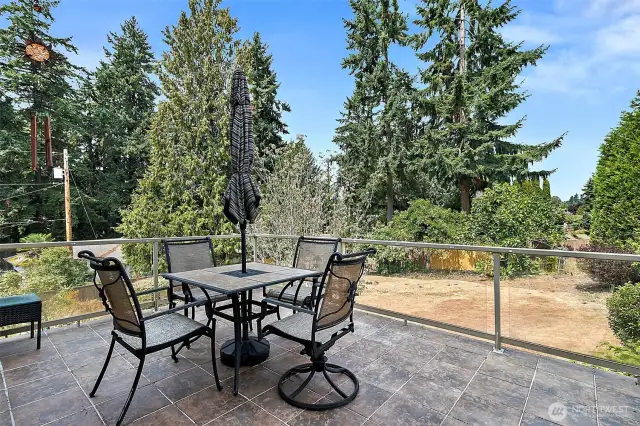A spacious deck off the kitchen and family room, featuring tile flooring and glass railings.  It offers uninterrupted views perfect for enjoying the outdoors in style.