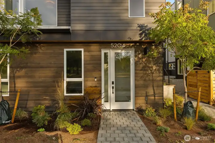 Welcoming entry framed by warm wood and greenery. A tidy walkway and layered plantings create an inviting first impression.