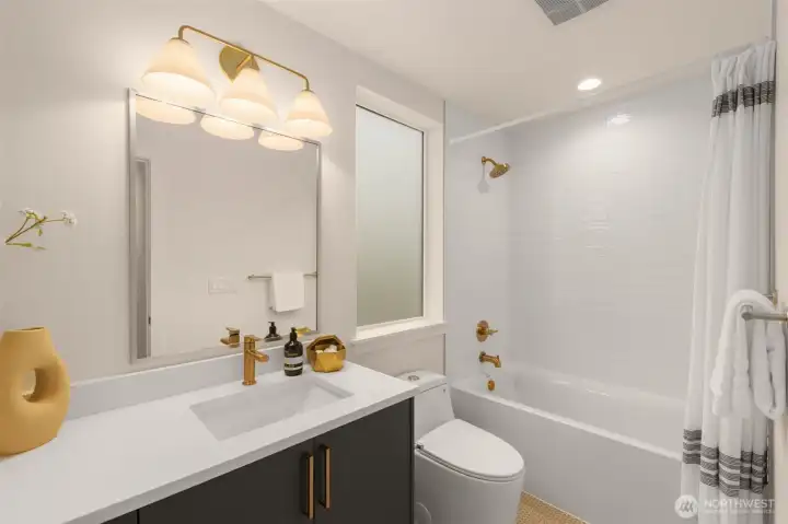 Polished secondary bath featuring a soaking tub, quartz topped vanity, and brass toned accents. Ideal for guests or a nightly wind down.