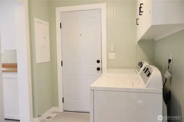 Efficient laundry room featuring a tankless water heater and extra cabinet storage above the washer and dryer.