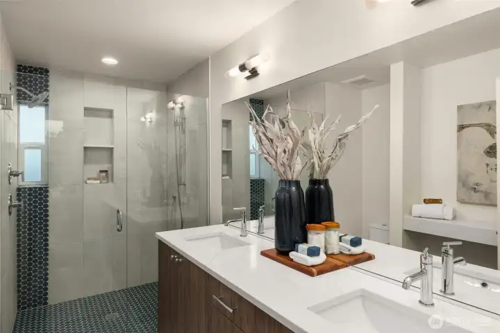 Pamper yourself in the beautifully designed ensuite bath, showcasing a sleek double vanity, luxurious finishes, and an expansive glass-enclosed shower—a space to indulge in ultimate comfort. Photos of home with similar layout, finishes & fixtures.
