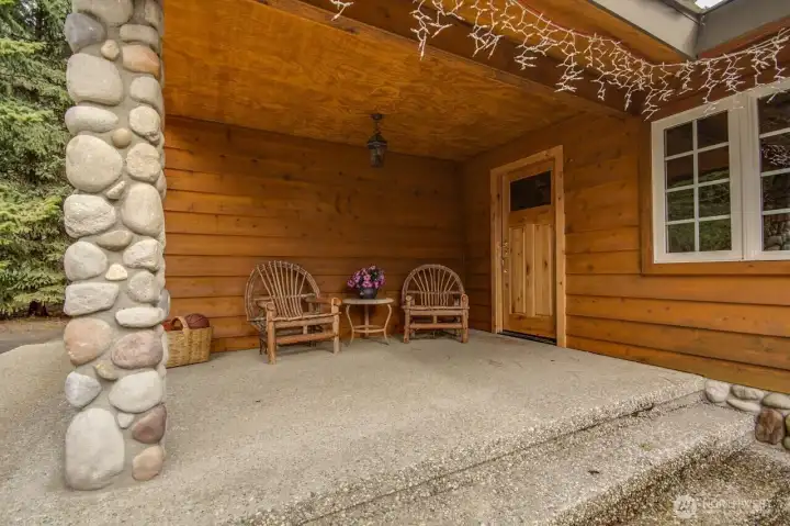 Charming covered entry featuring natural wood finishes, stone column, and a cozy seating area.