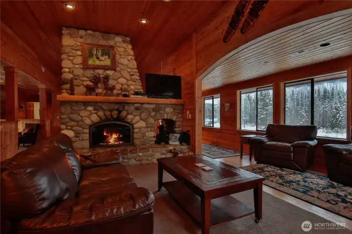 Inviting living room centered around a stunning river rock fireplace, with expansive windows showcasing the surrounding natural beauty