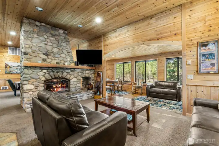 Inviting living room centered around a stunning river rock fireplace, with expansive windows showcasing the surrounding natural beauty