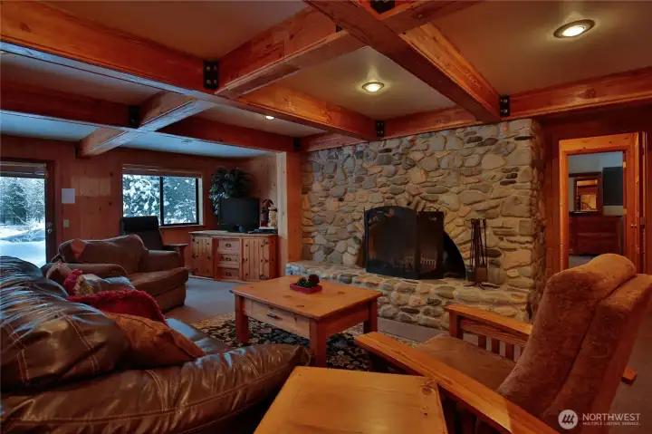 A beautifully crafted lower level lounge  with exposed beams and a dramatic river rock fireplace, embodying true alpine charm