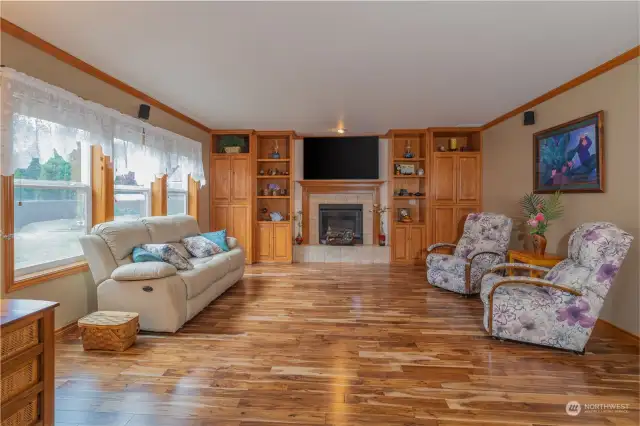 View from kitchen looking into the living room. Features propane fireplace, built-ins, hardwood floors and natural light