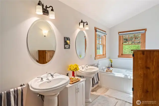 Spacious primary bathroom has a full shower, dual sinks, soaking tub, natural light, and doorway to main patio.