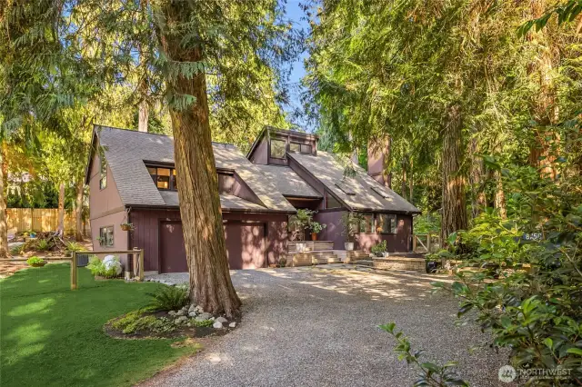 A gravel drive leads through established vegetation and ornamental maples to the home and attached 2-car garage