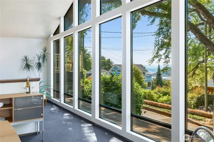 A wall of windows frames heritage trees and glimpses of Puget Sound, merging calm greenery with horizon views that stir a sense of wonder.