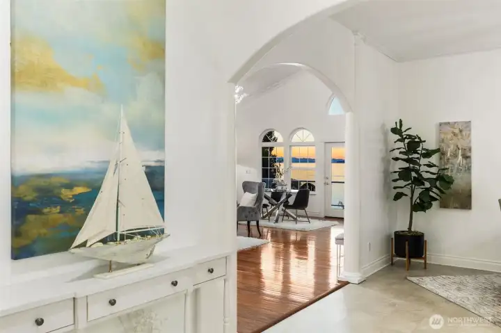 Bright and inviting entry with arched detailing, hardwood floors, and a serene coastal aesthetic leading to open-concept living with water views.