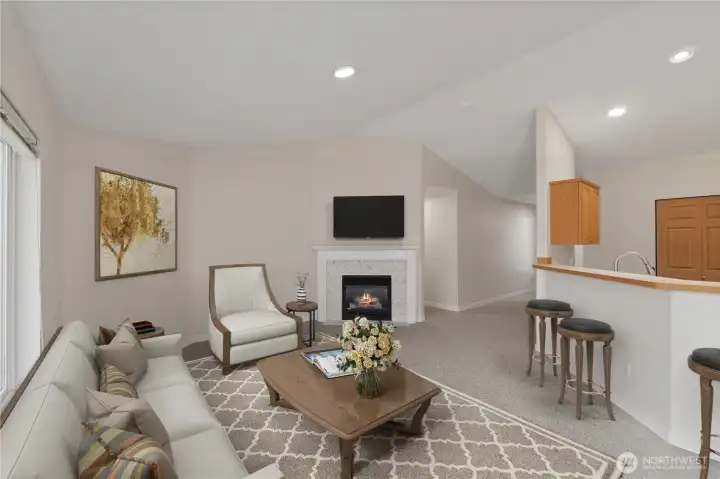 The open-concept design connects the living room and kitchen seamlessly, featuring vaulted ceilings, a cozy gas fireplace, and breakfast bar seating—ideal for gatherings and everyday comfort.