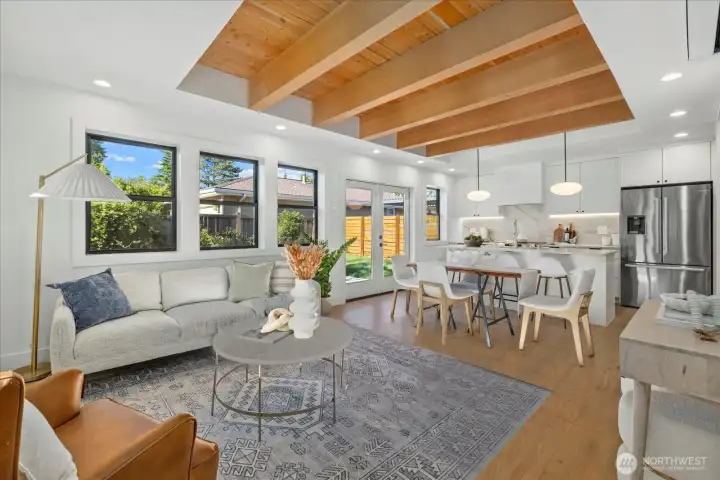 Open concept living room with exposed wooden ceiling, beautiful natural stone kitchen with full height backsplash, and easy access to the large yard.  Black, upgraded Milgard windows and ambiance and under-cabinetry lighting make this living room a wonderful space to relax or entertain.