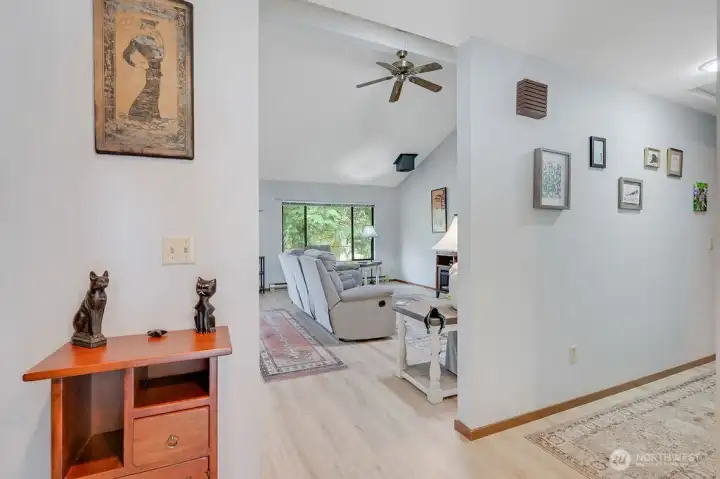 The entry opens to a spacious open area, with vaulted living and dining areas. The hallway leads to the primary bedroom.