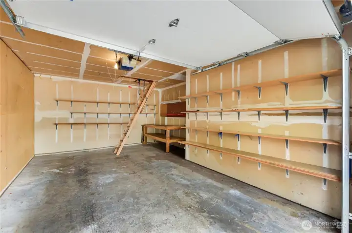 The one-car garage has storage space along the walls, a work bench, and pull-down stairs to attic storage space.