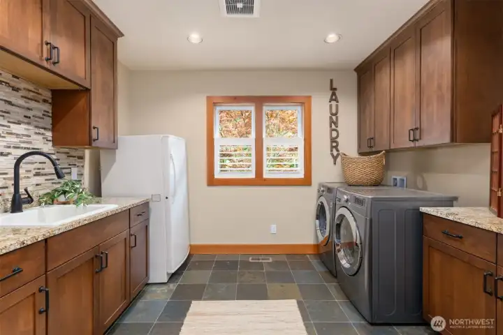 The utility room is a dream, with side-by-side washer and dryer, a laundry sink, counter space, storage, and an upright freezer.