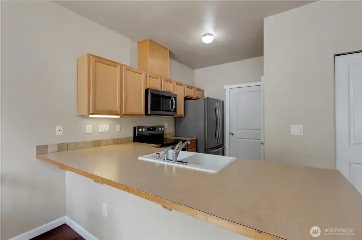 Kitchen featuring stainless steel appliances, maple cabinetry, and tile backsplash, highlighted by a spacious eating bar ideal for casual meals and gathering.