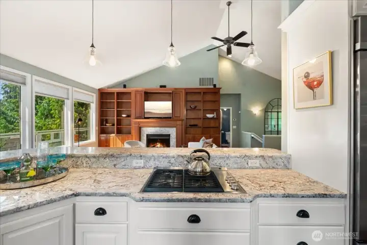 The open-concept kitchen and great room blend style and function, featuring quartz countertops, white cabinetry, stainless steel appliances, pull-out cabinet storage, and a welcoming gas fireplace surrounded by custom built-ins.