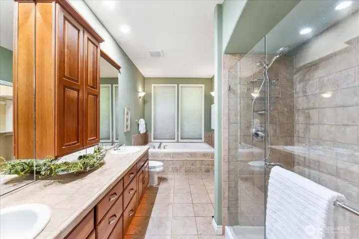 This beautifully appointed primary bath offers floor to ceiling tiled walk-in shower, elegant under- vanity lighting, dual sinks, tiled flooring and jacuzzi tub.