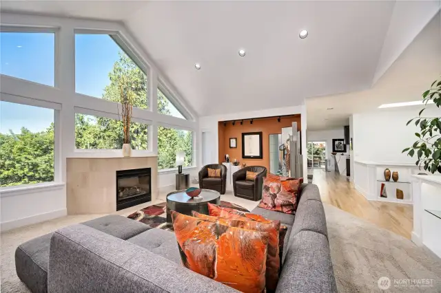 The main living space with vaulted ceilings and views of the Olympics and woodlands. Down the hallway is the dining room on the left and the kitchen to the right. The sliding door in the background leads to the partially covered deck.