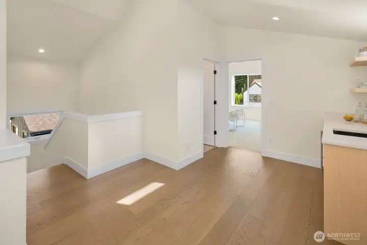 This photo shows the landing at the top level of the home. On the right is a wet bar with a beverage fridge. There's a full bath through the door on the left and the back room is another bedroom with two huge storage closets.
