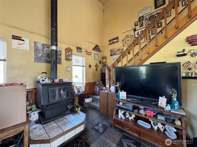 Living room with vaulted ceilings, wood stove and stairs to upper level.