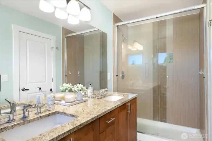Large primary en-suite bath with dual vanities, ample cabinetry and beautiful tilling in the shower.