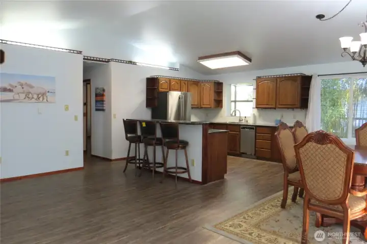 The view of your new home from the front door showing vaulted ceilings in the open concept living area and island seating in the kitchen!  The home features Luxury Vinyl Plank flooring throughout!