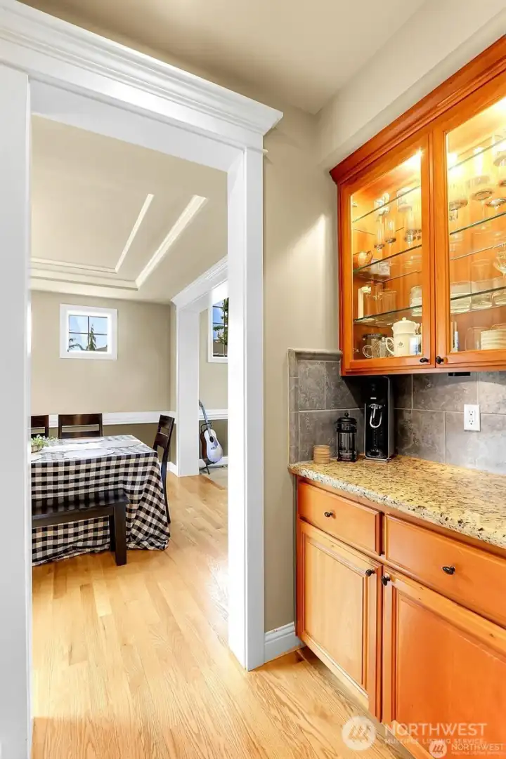 Butlers pantry with granite counters and tile backsplash located between chef's kitchen and formal dining room.