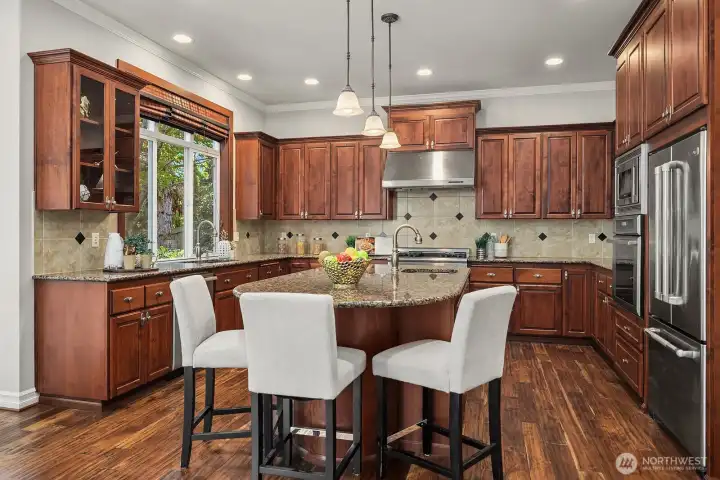 This angle showcases the kitchen's thoughtful layout, highlighting the generous cabinetry, premium stainless steel appliances, and a stylish tile backsplash that adds a refined finishing touch. The island's clean lines and comfortable bar seating make this space equally suited for quick morning breakfasts or hosting elegant gatherings.
