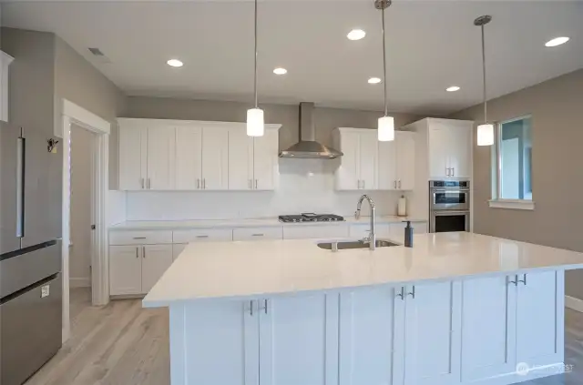 The kitchen island features hidden extra cabinets beneath the sleek Quartz countertop.