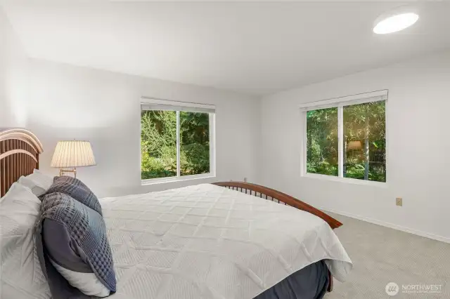 Primary bedroom is king size space with windows overlooking the lush greenery.