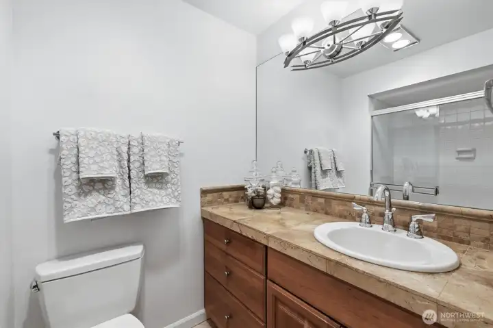 En-suite primary bath with upgraded vanity, tile countertop, & newer lighting.