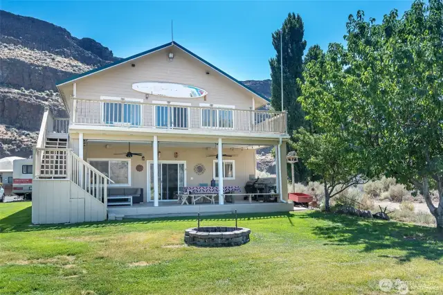 Back of the house, 2 stories with the covered deck and large eating area. Stairs do lead up to the second floor with big deck that can hold lots of star gazers entertaining friends. Big grass yard with a fire pit and a plum tree.