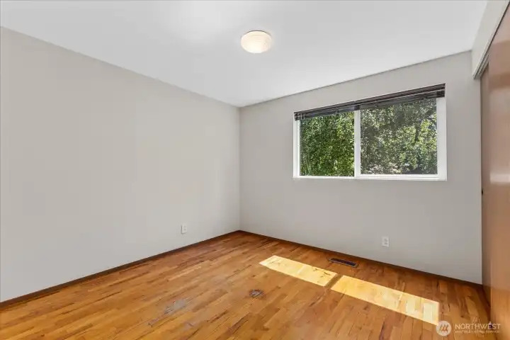 Bright upstairs third bedroom with hardwood floors and peaceful natural views through the large window Bright upstairs third bedroom with hardwood floors and peaceful natural views through the large window