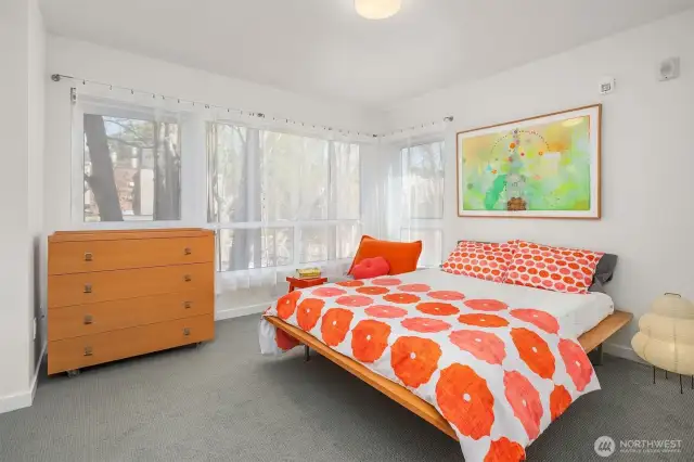 Primary bedroom. Bright light from windows that wrap the room.  Shown here are all cotton Voile draperies for soft light. At night draw the cellular shades for privacy. There is a dual closet on the side of the room not seen, fitted with interior sections.