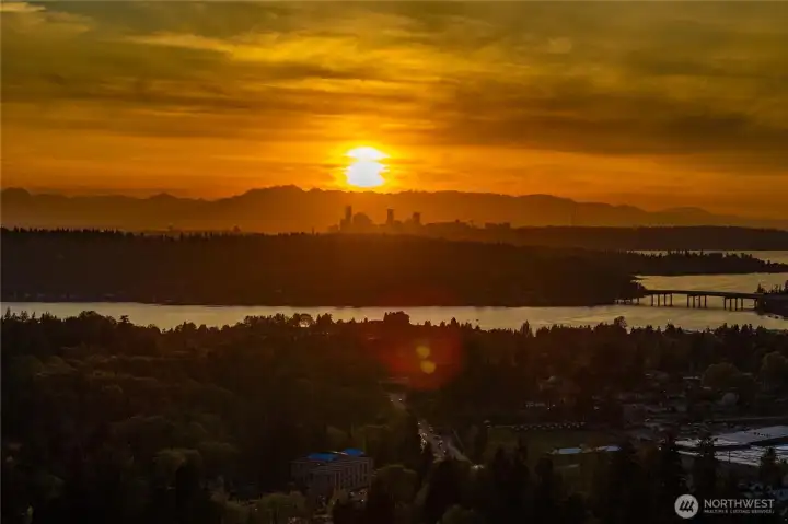 A wide-angle view overlooking the lake as the I-90 bridge stretches toward the sun-drenched towers of Bellevue and the iconic Seattle skyline.