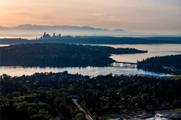 A wide-angle view overlooking the lake as the I-90 bridge stretches toward the sun-drenched towers of Bellevue and the iconic Seattle skyline.