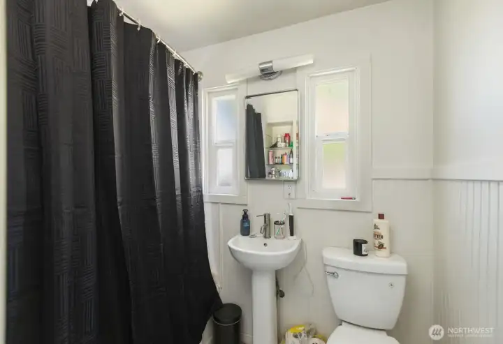 Bathroom includes a pedestal sink, ample natural light, and convenient access to nearby bedrooms.