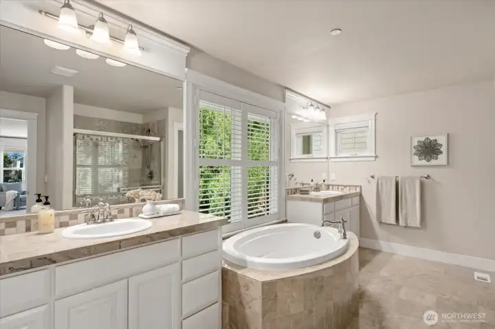 Spa-like primary bathroom with marble tiling, dual vanities, separate shower, and a large soaking tub! Green views from this space enable a quiet solitude.